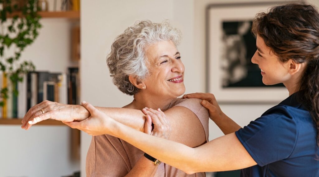 Happy senior woman doing exercise at home with physiotherapist